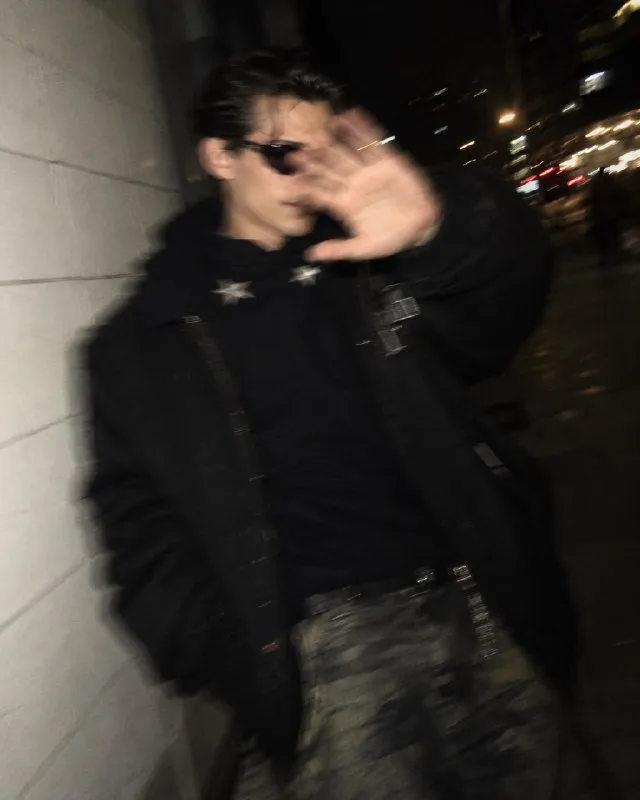 Random candid nighttime selfie, 4:5 aspect ratio. A person wearing a black coat and black sunglasses